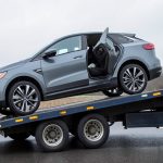 An electric car being loaded onto a flatbed tow truck at the roadside with its charge port visible
