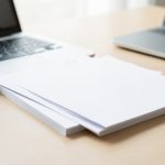 Several document pages merging into a single stacked PDF file icon on a laptop screen