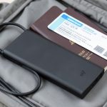 A power bank and charging cable next to a passport and boarding pass in an open carry-on bag