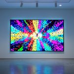 A large glowing screen showing abstract colorful generative digital art in a minimal gallery