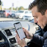 A used car buyer comparing a vehicle's odometer reading against a history report on a phone