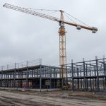 A stalled construction site with a steel framework and a tall crane under an overcast sky