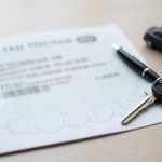 A car title document and pen on a table with car keys, representing transferring a vehicle title in a private sale