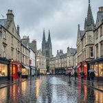 A rainy cobbled street in Edinburgh's Old Town with historic stone buildings and people carrying umbrellas