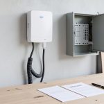 A homeowner comparing two EV charger installation quotes on paper next to a wall-mounted home charging unit in a garage
