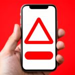 A smartphone showing a fake alarming virus warning pop-up with a warning symbol, representing a scareware scam