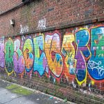 A brick building wall covered in colorful spray-paint graffiti tags in an urban alley