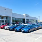 A row of new cars parked on a dealership lot under a clear sky
