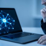 A person thinking while looking at a laptop displaying an abstract glowing AI network graphic