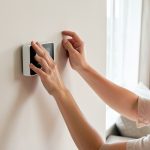 A homeowner adjusting a wall-mounted smart thermostat in a bright living room