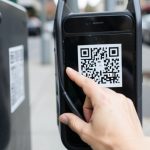 A hand scanning a QR code sticker on a parking meter with a phone, illustrating a potential QR-code parking scam