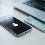 A phone showing a locked account screen next to a laptop, representing recovering an Apple Account without a trusted phone number