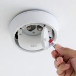 A ceiling-mounted round smoke alarm with its battery cover open, representing troubleshooting a chirping smoke alarm