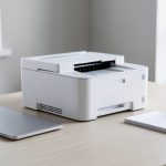 A home office inkjet printer on a desk beside a laptop, representing a printer subscription buying decision