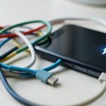 A tangle of different USB-C cables next to a phone showing a charging icon, illustrating cables that charge slowly or not at all