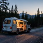 A camper van parked at dusk on a gravel forest road near tall pines at the edge of a national park