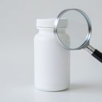 A magnifying glass held over a blank supplement bottle label on a table, suggesting scrutiny of weight-loss product claims