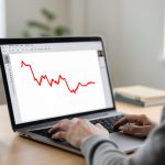 A calm person at a laptop showing a red stock chart declining from upper left to lower right