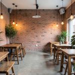 A minimalist cafe interior with exposed brick, Edison bulb lights, reclaimed wood tables, and potted plants